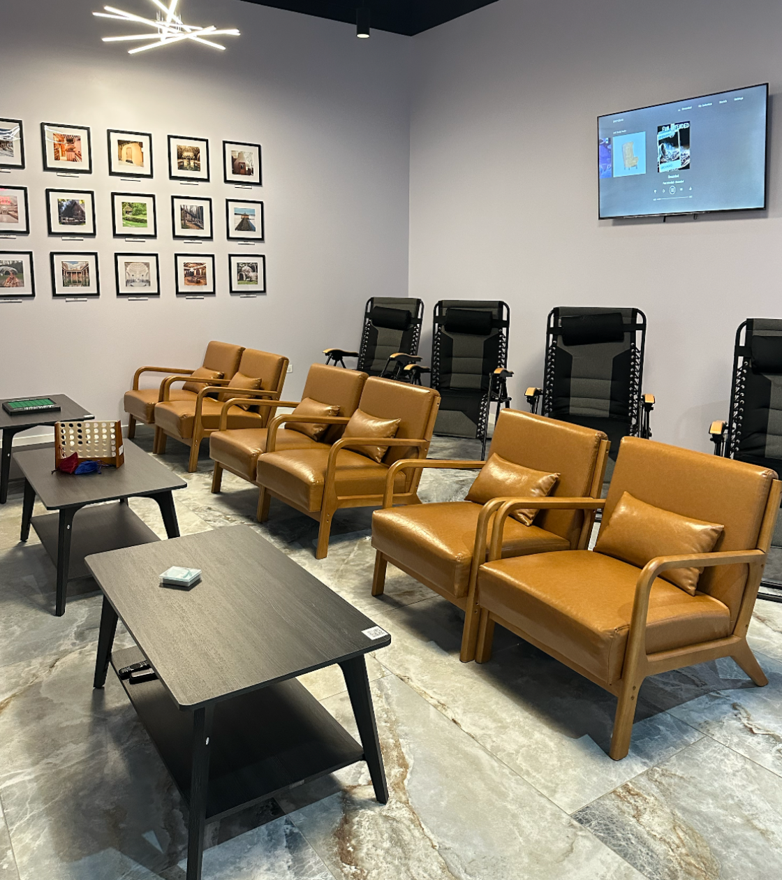 Modern waiting room with brown chairs, black tables, and a wall-mounted TV.